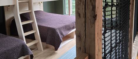 Habitación con literas, una escalera, una ventana con vistas y suelo de madera.