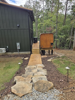 A wooden deck leading to a building with a green exterior, surrounded by a forested area with stone pathways and small lights. - Reconnect with nature and family in this one-of-a-kind stay at the Tableview. (Pickens)
