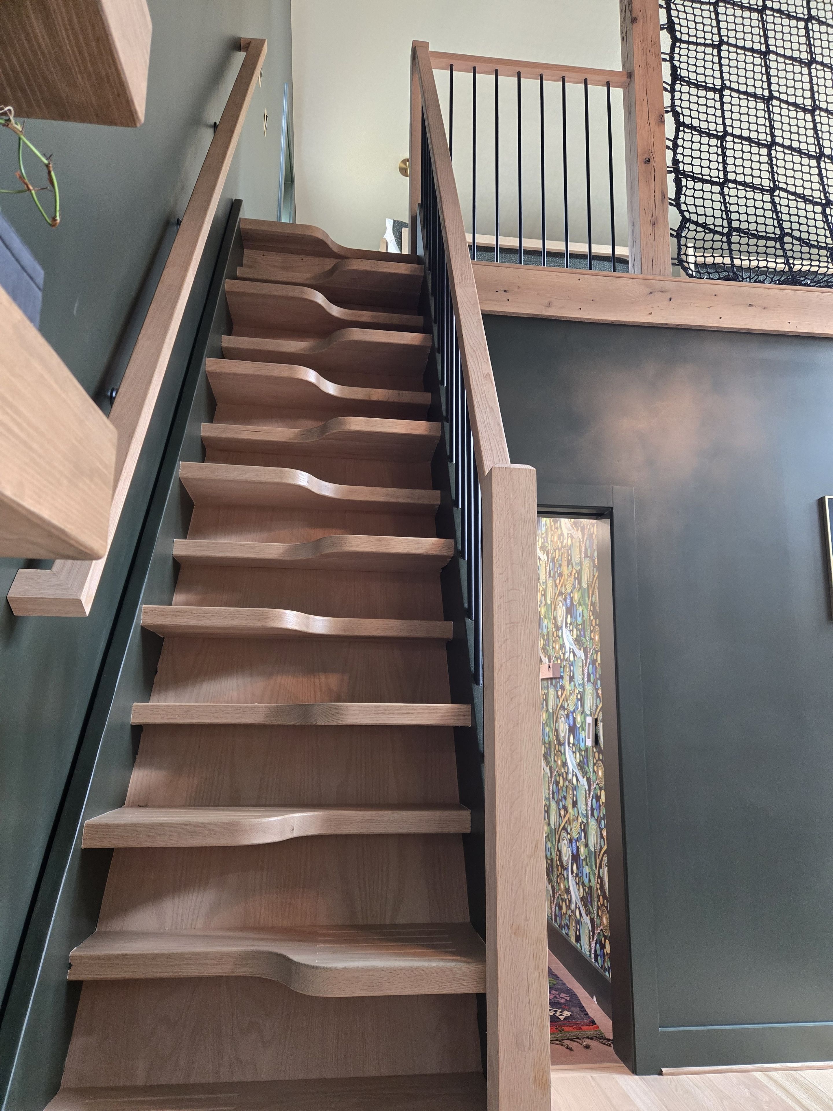 Una escalera de madera con barandal negro que conduce a una habitación con pared estampada y una puerta.