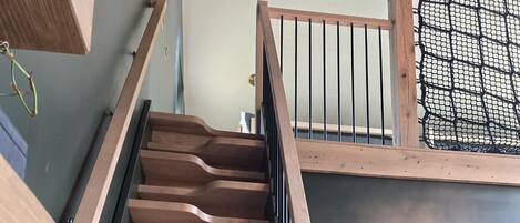 Una escalera de madera con barandal negro que conduce a una habitación con pared estampada y una puerta.