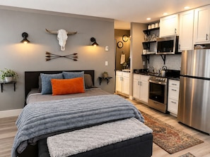 Un dormitorio moderno con una cama grande, una cocina con electrodomésticos de acero inoxidable y decoración mural.