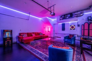A room with a red sofa, a blue armchair, a patterned rug, and arcade games. - Pink Vibes! Hot Tub + Rooftop Views  Sleeps 16 (Nashville)