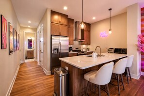 A modern kitchen with a stainless steel refrigerator, wooden cabinets, a marble countertop, and a bar area with white chairs. - Pink Vibes! Hot Tub + Rooftop Views  Sleeps 16 (Nashville)