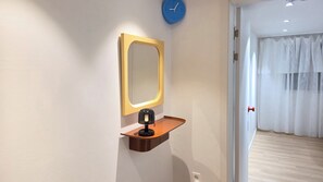 Ein Zimmer mit einem an der Wand befestigten Spiegel, einer Uhr und einem kleinen Regal mit einer Lampe.