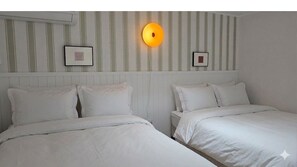 Hotellihuone, jossa on kaksi sänkyä, seinään kiinnitetty valaisin ja kehystetyt valokuvat.