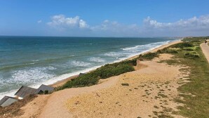 Una playa costera con cielo despejado, un sendero arenoso y vista al océano.