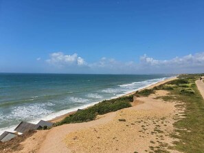 Ein Küstenstrand mit blauem Himmel, einem Sandweg und Blick auf den Ozean.