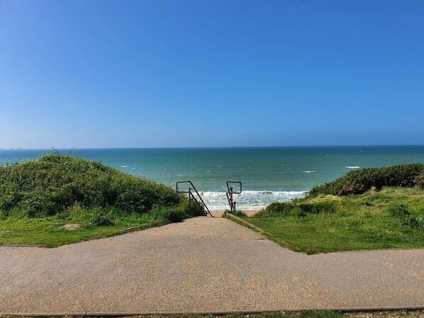Ein gepflasterter Weg führt zu einem Strand mit freiem Blick auf das Meer.