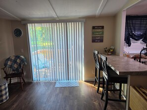 Un comedor con barra de cocina, sillas, un reloj y vistas a través de un puerta corredera.