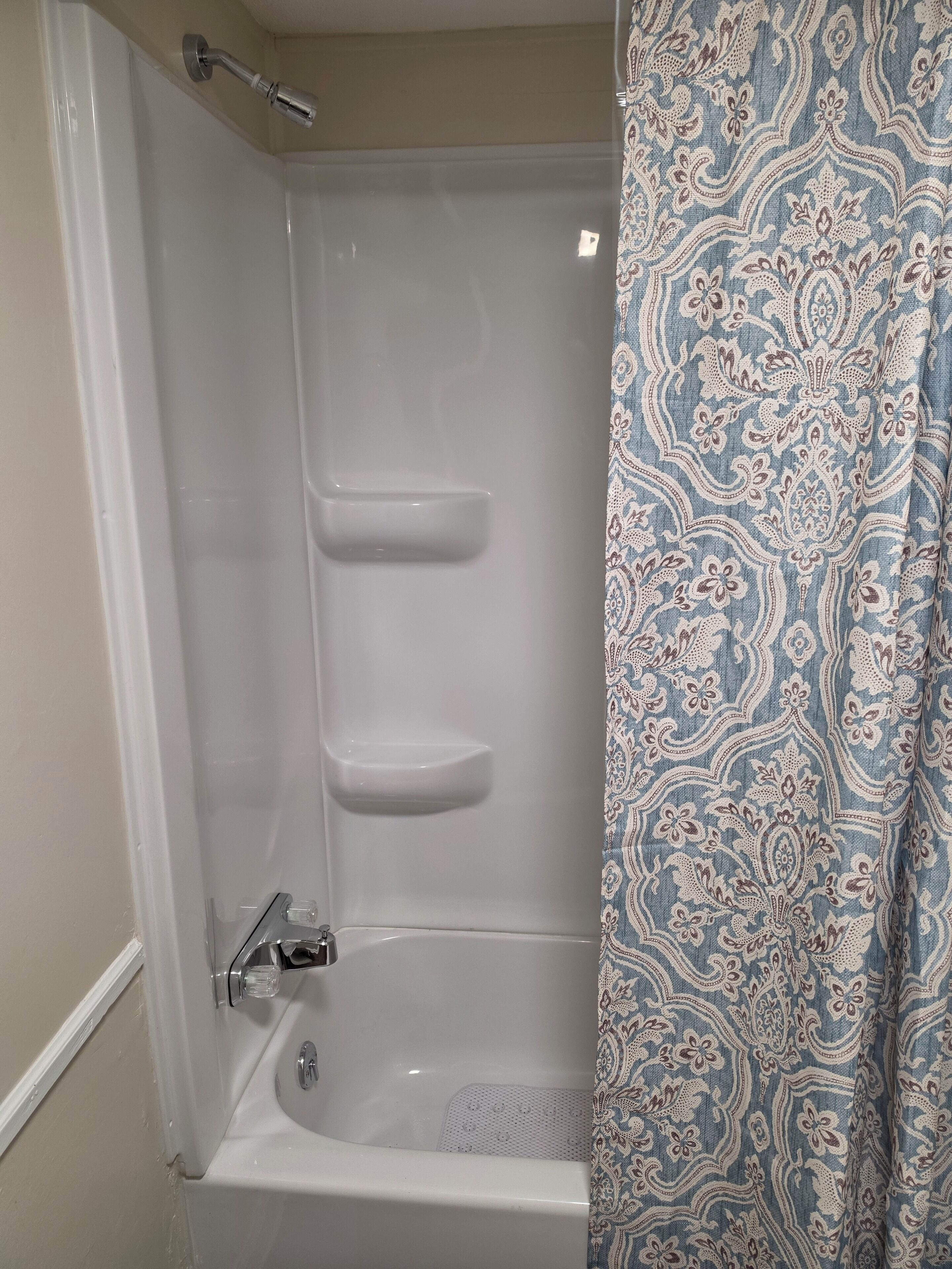 Una ducha con puerta de vidrio, cortina de baño con estampado de cachemir y una bañera blanca.
