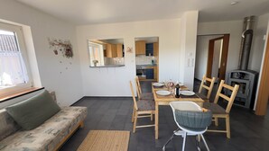 A modern living room with a sofa, dining table, chairs, a fireplace, and a kitchen in the background. - MainNest Marktbreit - Family Apartment (Marktbreit)