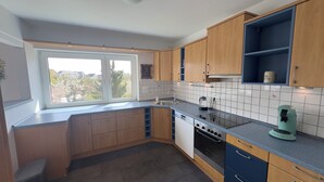 A kitchen with wooden cabinets, a dishwasher, an oven, a window, and a view of houses. - MainNest Marktbreit - Family Apartment (Marktbreit)