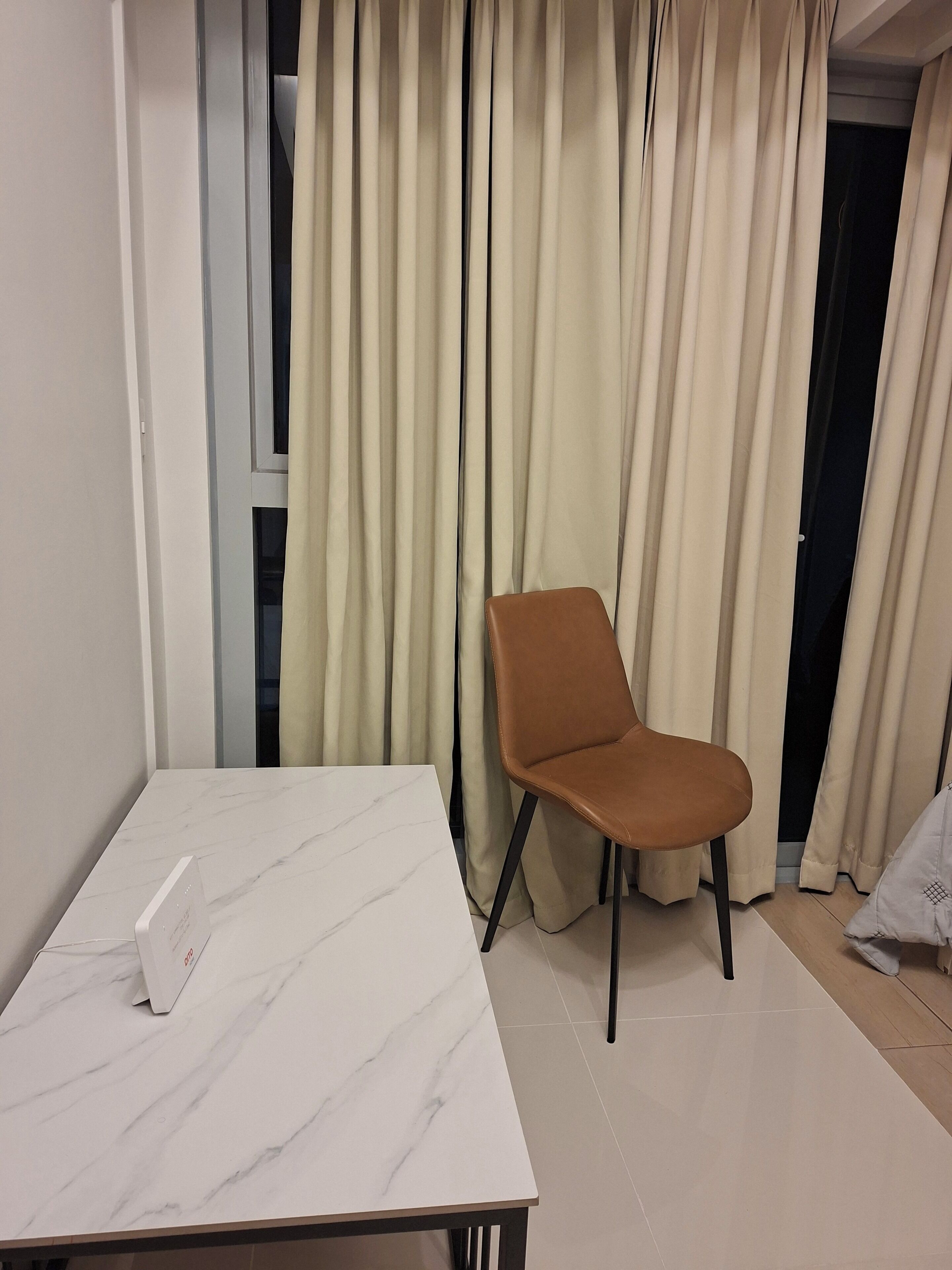 Une pièce avec une table en marbre, une chaise marron et des rideaux beige.