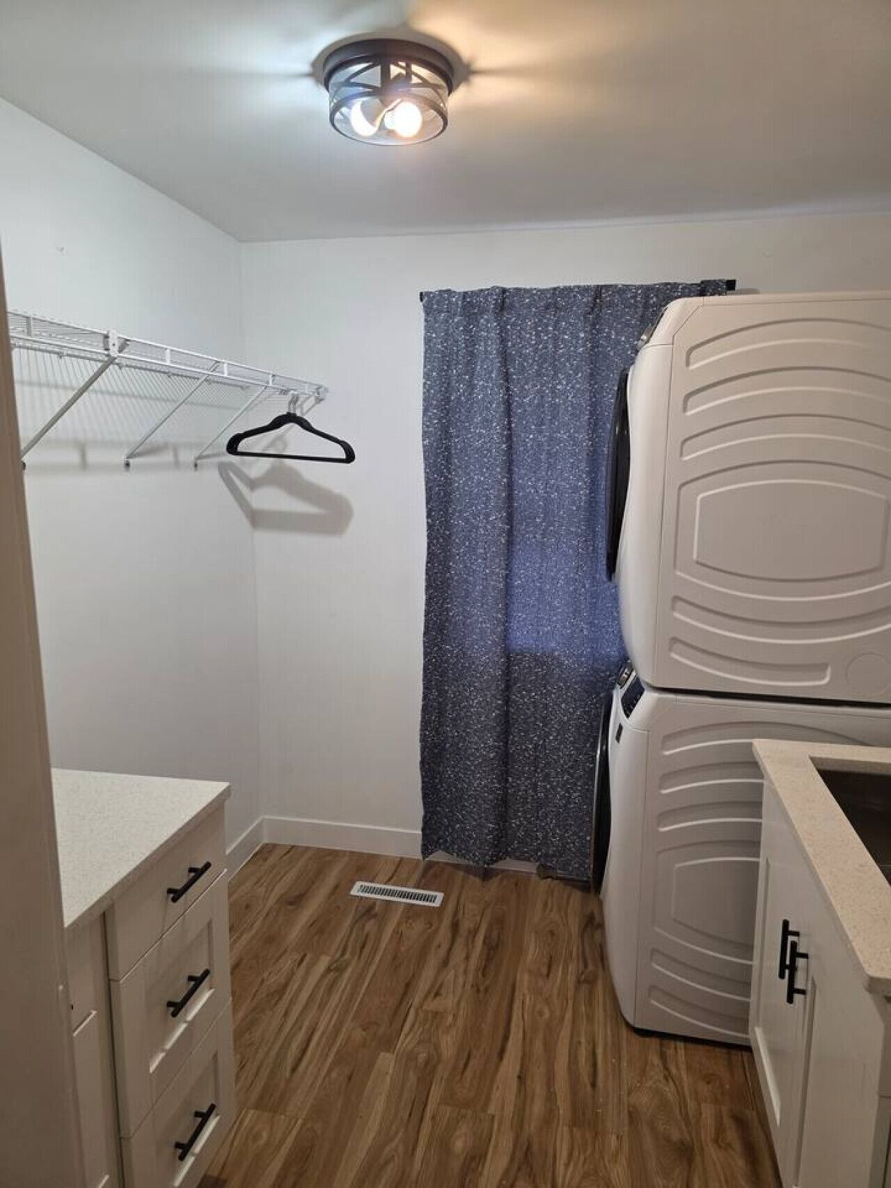 A compact room with a wooden floor, a white wardrobe, a drying rack, and a shower curtain.