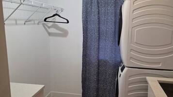 A compact room with a wooden floor, a white wardrobe, a drying rack, and a shower curtain.