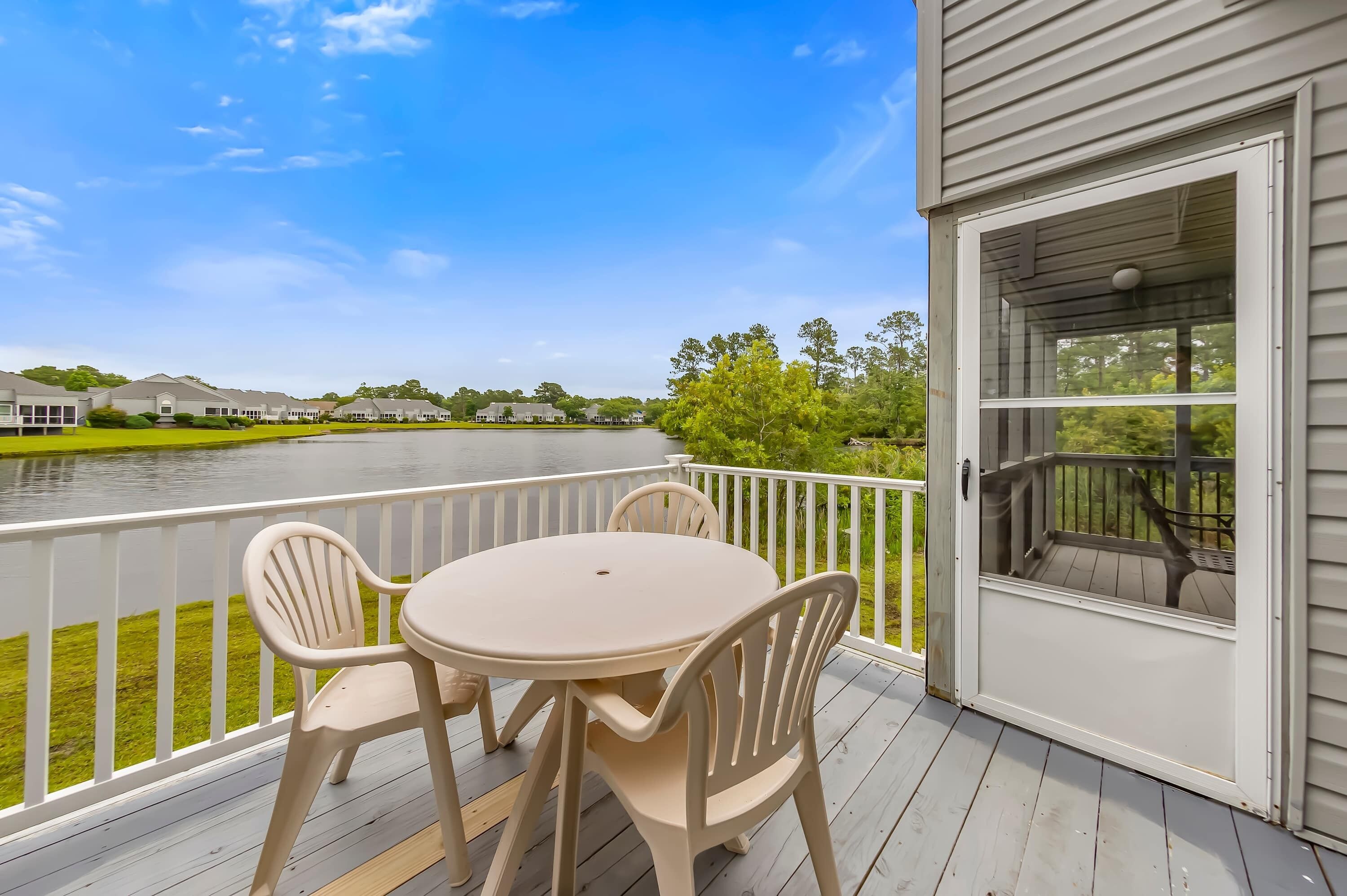 A deck with a table and chairs overlooking a body of water and a row of houses.