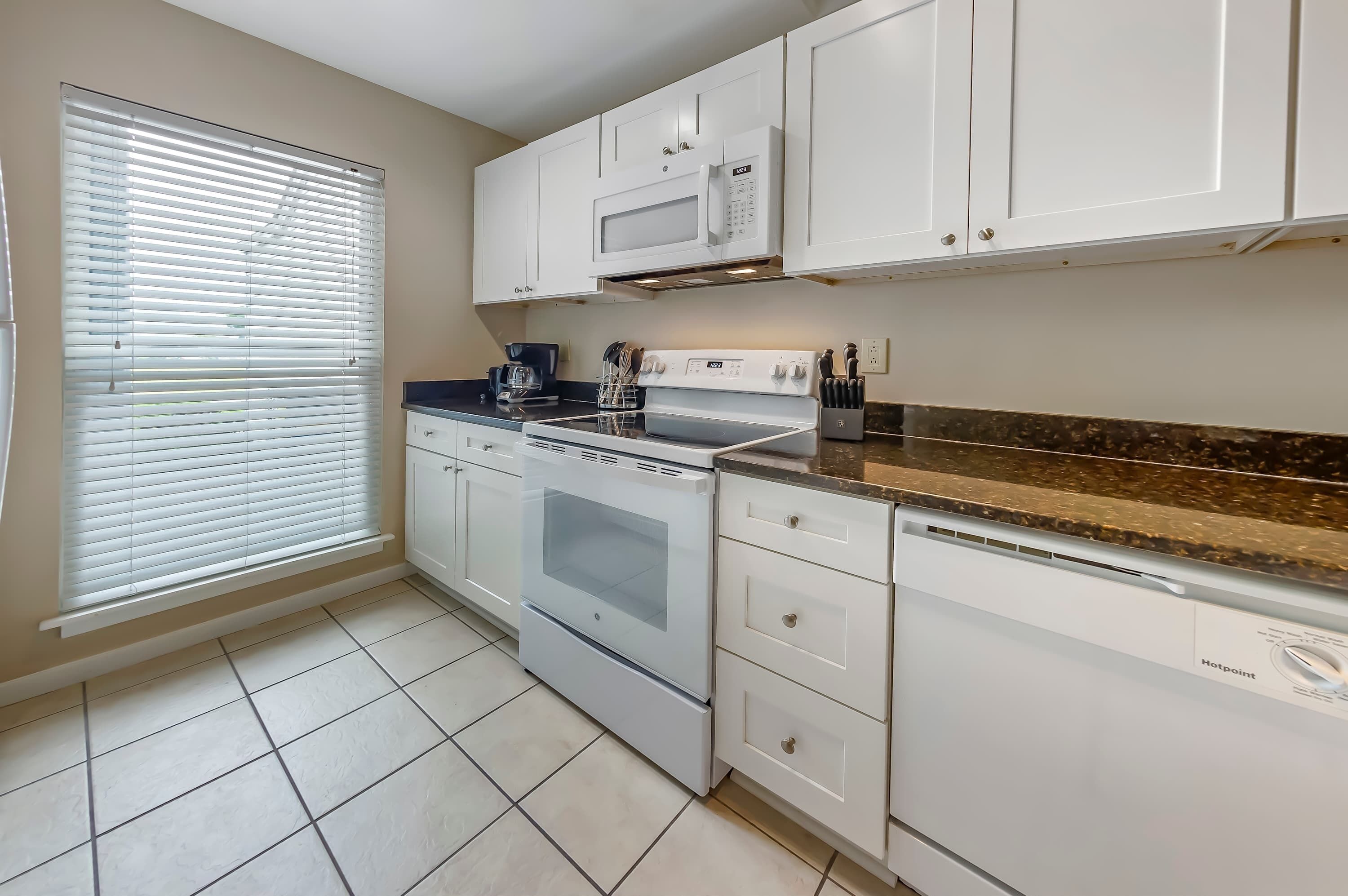A kitchen with white cabinets, a microwave, an oven, a dishwasher, and a window with blinds.
