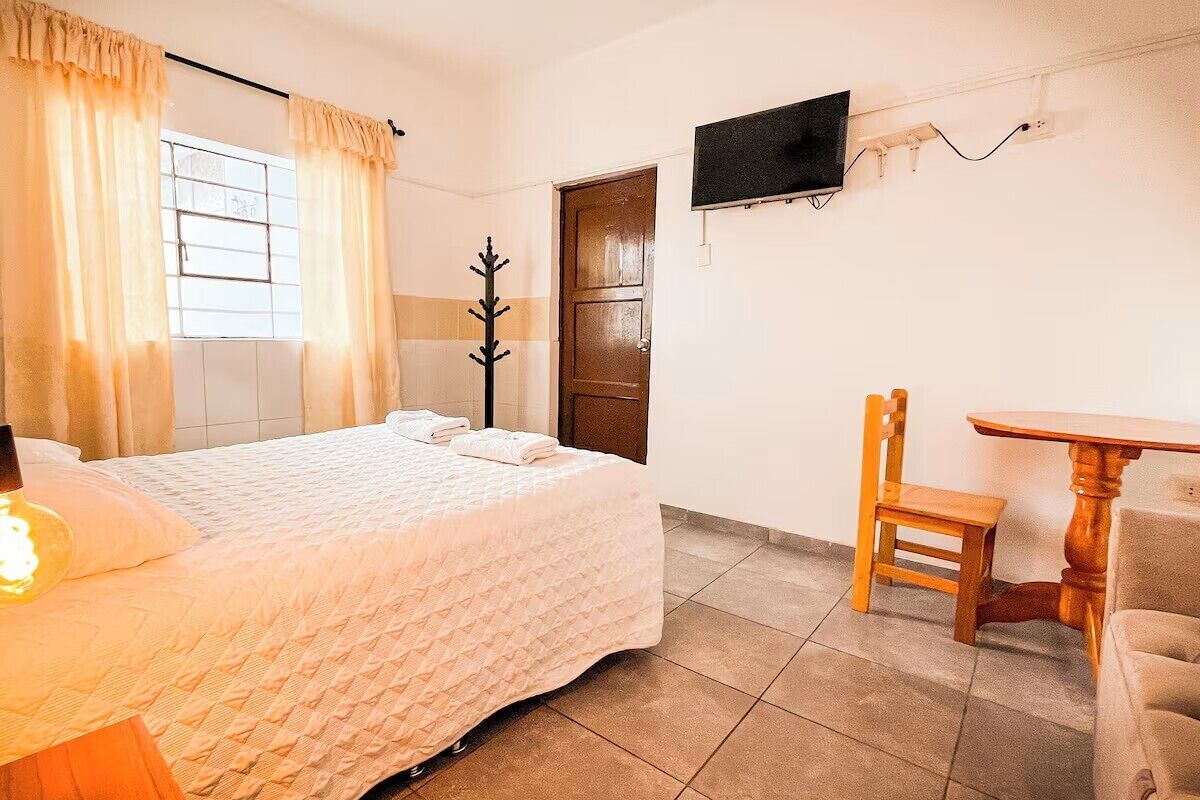A hotel room with a bed, a TV mounted on the wall, a wooden chair, and a small table.