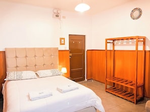 A hotel room with a bed, a wooden wardrobe, a bedside table with a lamp, and a wall clock. - Casona de San Agustin (Cusco)