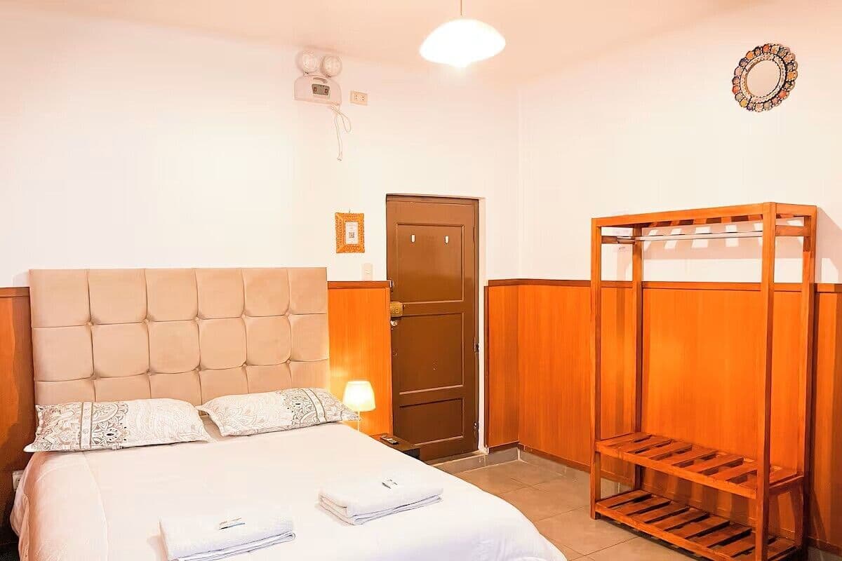A bedroom with a bed, a wooden wardrobe, a door, and a wall-mounted light fixture.