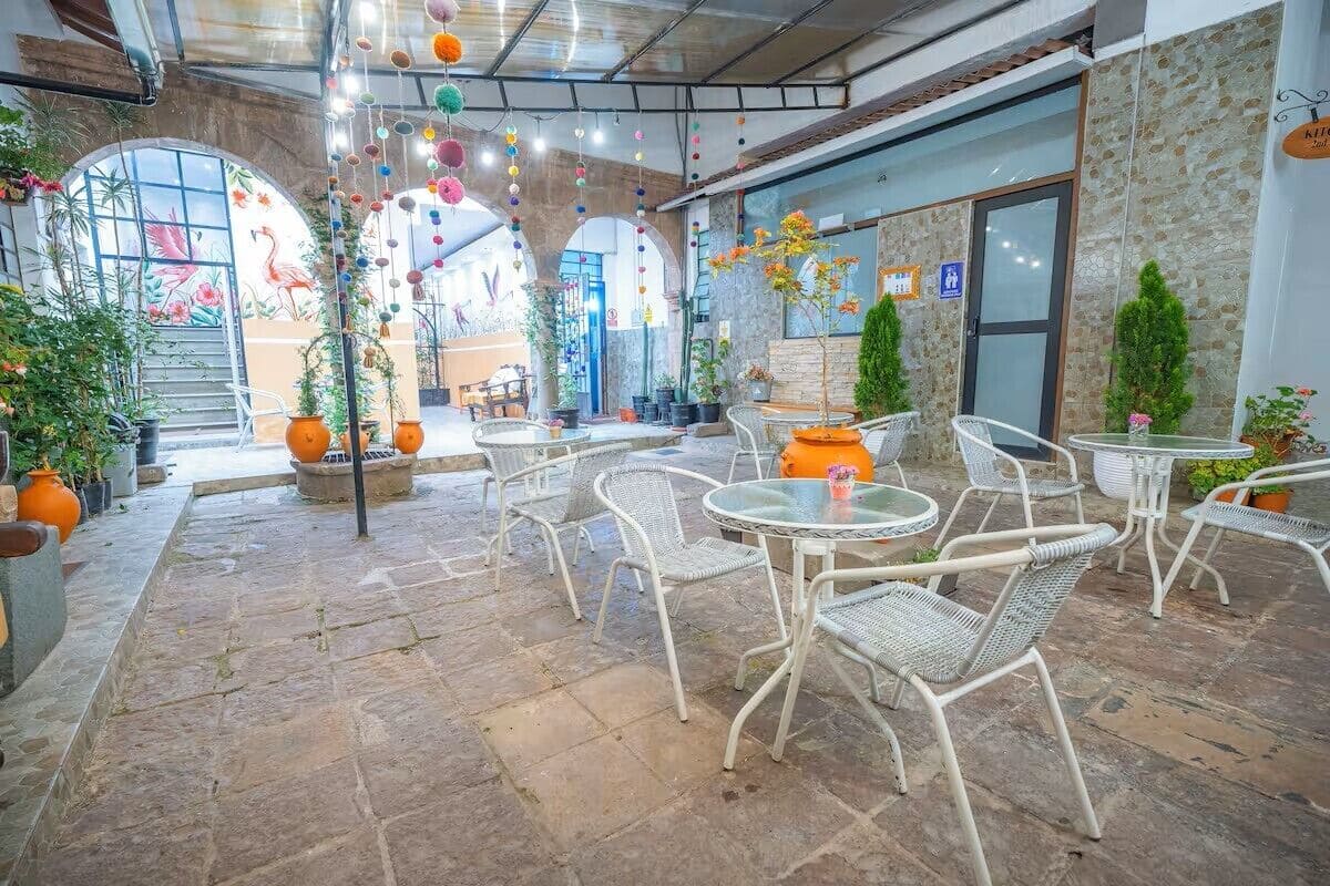 A covered outdoor seating area with wicker chairs and tables, potted plants, and a stone floor.