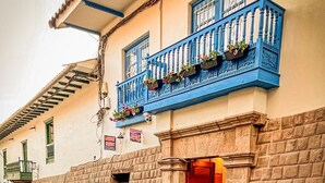 A building with a stone facade, a red door, and a blue balcony with flowers. - Casona de San Agustin (Cusco)