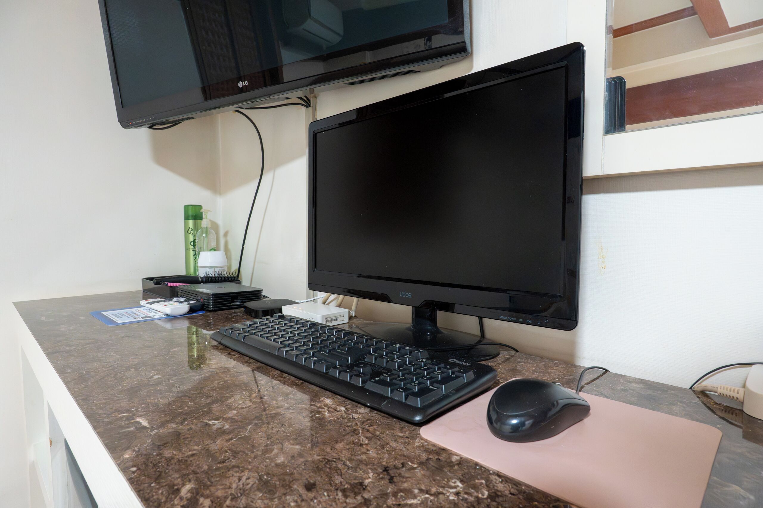 A computer desk with a monitor, keyboard, mouse, and a pink mouse pad.