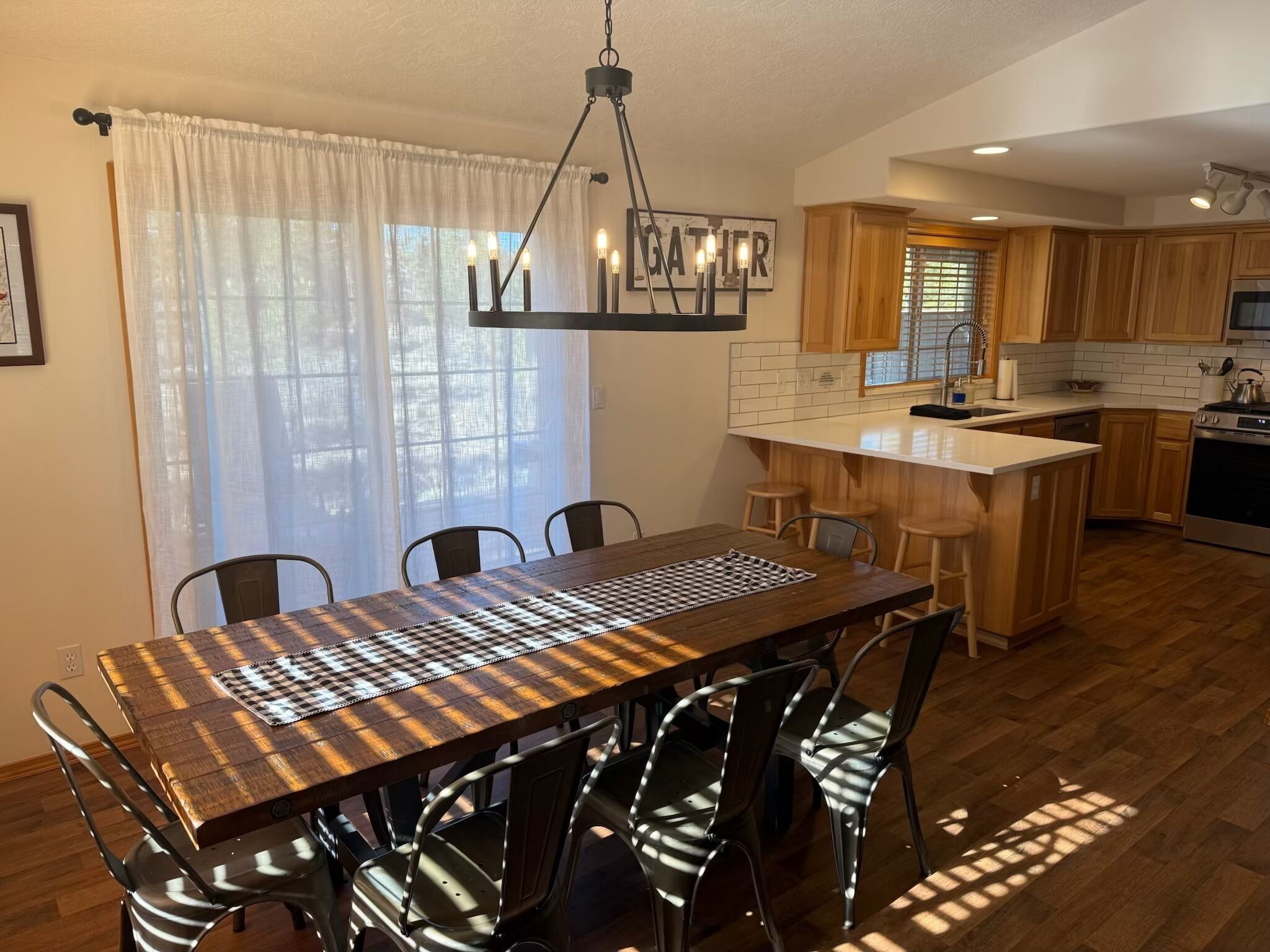 A modern kitchen with wooden cabinets, a central island, and a dining area with a checkered tablecloth.
