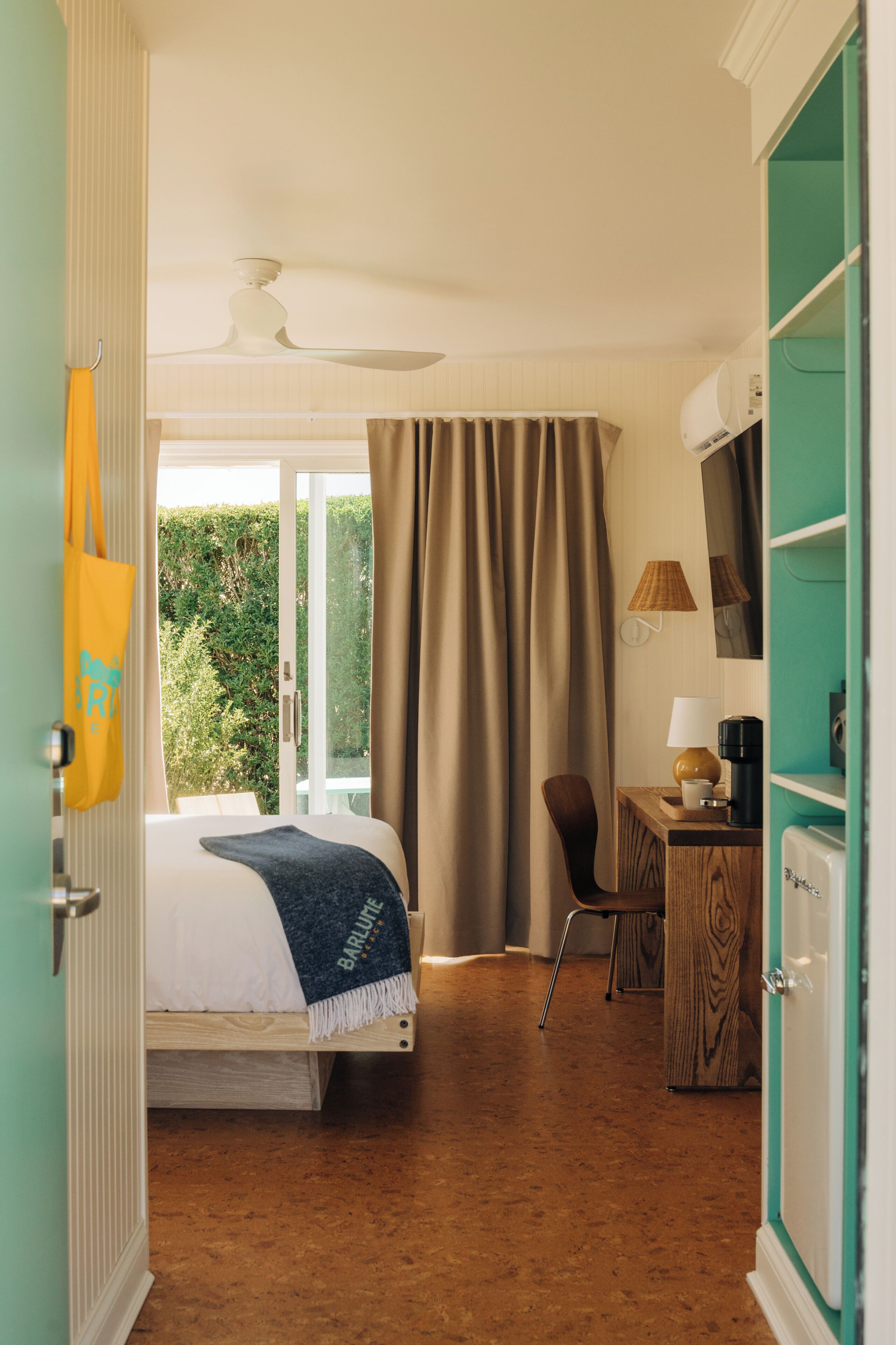 A hotel room with a bed, a desk, a chair, a coffee maker, and a view of greenery outside.