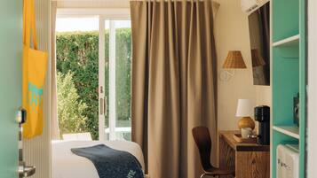 A hotel room with a bed, a desk, a chair, a coffee maker, and a view of greenery outside.