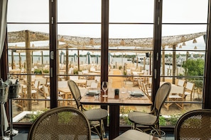 A restaurant with outdoor seating overlooking a body of water, featuring wicker chairs and tables. - Barlume Beach Montauk (Montauk)