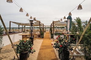An outdoor seating area with tables and chairs, a sandy path, and potted plants. - Barlume Beach Montauk (Montauk)