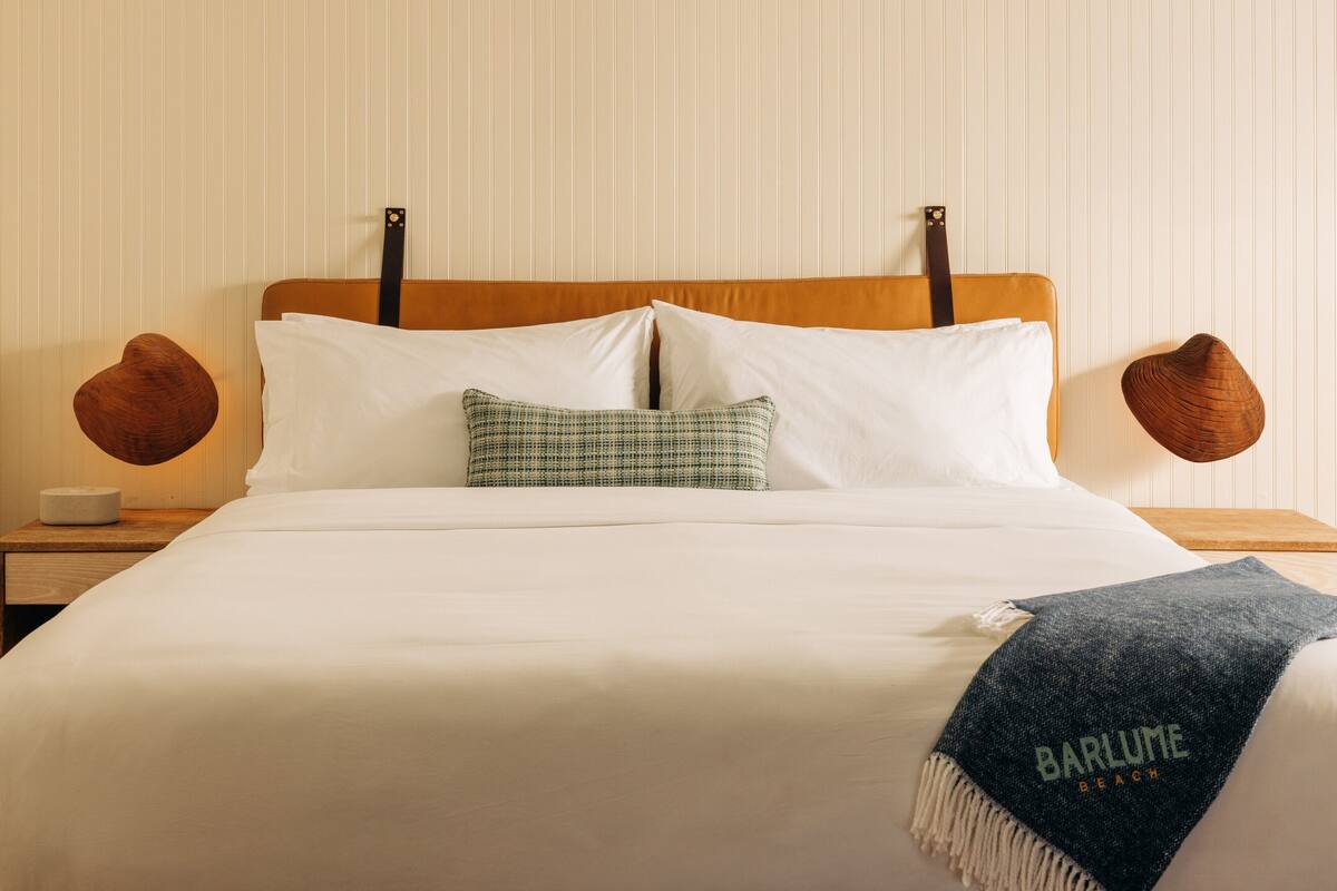 A neatly made bed with white linens, a checkered pillow, and a blue throw blanket with text.