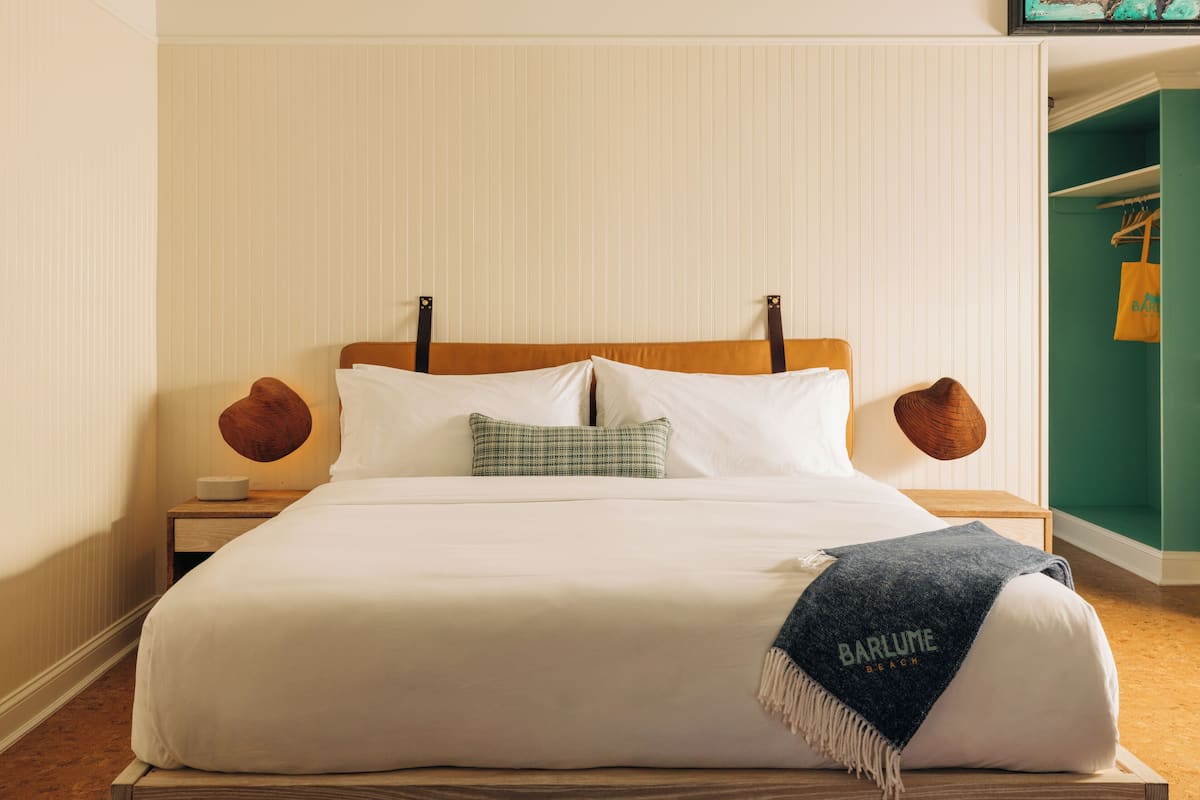 A neatly made bed with a white comforter, two pillows, a plaid throw pillow, and a blue throw blanket with text.