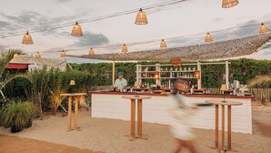 Zona de bar al aire libre con toldo, mesas y un cantinero.
