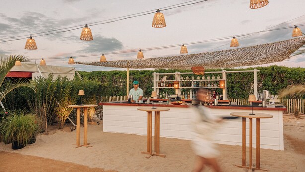 An outdoor bar area with a canopy, tables, and a bartender. - Barlume Beach Montauk (Montauk)