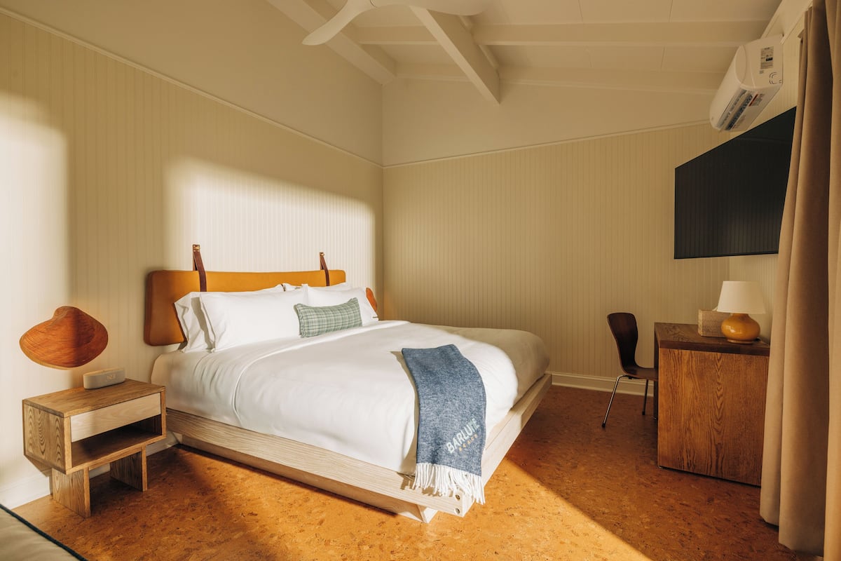 A bedroom with a bed, bedside table, chair, desk, and an air conditioning unit.