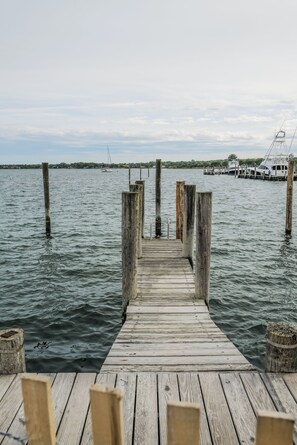 A wooden pier leading into calm waters with boats docked in the background.