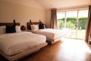 Quarto de hotel com duas camas, uma grande porta de correr de vidro para o exterior e vista para o verde.