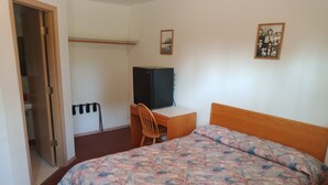 Een slaapkamer met een bed, een bureau, een stoel, een kledingkast en een schilderij aan de muur.