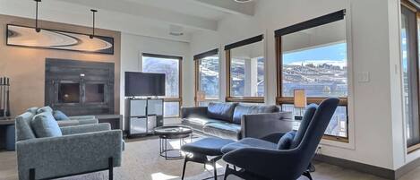 A modern living room with a fireplace, large windows, and a view of a snowy landscape.