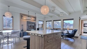 Une cuisine moderne dotée d’un îlot central, de grandes fenêtres et d’un coin repas avec des chaises.