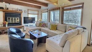 A living room with a sofa, chairs, a coffee table, a fireplace, a TV, and large windows. - The Plaza 239 | Walk to CBMR Lifts | 2 Hot Tubs+Sauna | 3BR Sleeps 8 (Crested Butte)