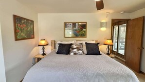 A bedroom with a bed, two bedside lamps, a ceiling fan, a window, and a door. - The Plaza 239 | Walk to CBMR Lifts | 2 Hot Tubs+Sauna | 3BR Sleeps 8 (Crested Butte)