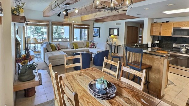 A spacious living area with a wooden dining table, a sofa, and a kitchen in the background. - The Plaza 239 | Walk to CBMR Lifts | 2 Hot Tubs+Sauna | 3BR Sleeps 8 (Crested Butte)