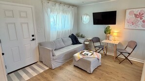Un salon comprenant un canapé, un pouf, des fauteuils, un téléviseur et une petite table avec une lampe.