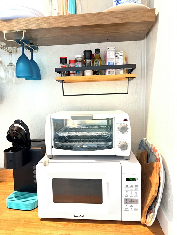A kitchen with a toaster oven, a coffee maker, and a shelf with various kitchen items. - Fay's Periwinkle Bungalow, Perfert for Couples (Bolivar Peninsula)