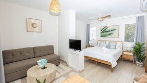 A modern hotel room with a sofa, bed, TV, ceiling fan, and large windows. - Modern Studio Pool Coral Azul Estrella Dominicus (Dominicus)