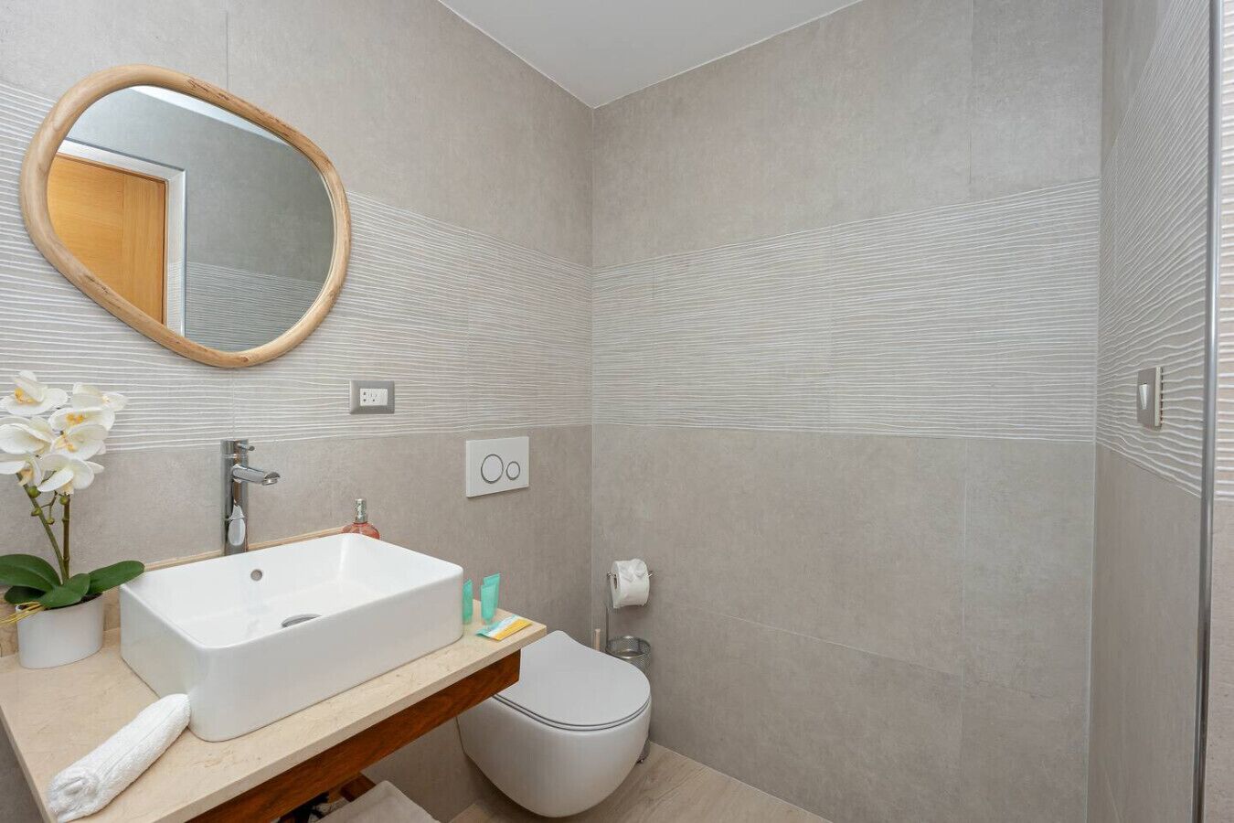 Et moderne badeværelse med en rektangulær vask, et rundt spejl, et toilet og et bruseområde.