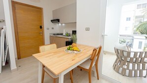 A modern kitchen with white cabinets, a wooden dining table with chairs, and a fruit bowl on the table. - Modern Studio Pool Coral Azul Estrella Dominicus (Dominicus)